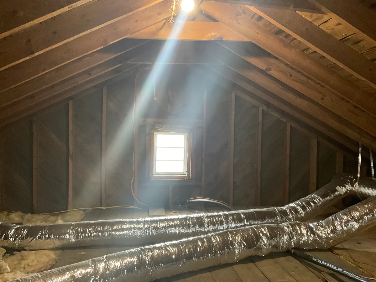 Accessible attic with exposed roof framing, insulated ductwork and a gable window