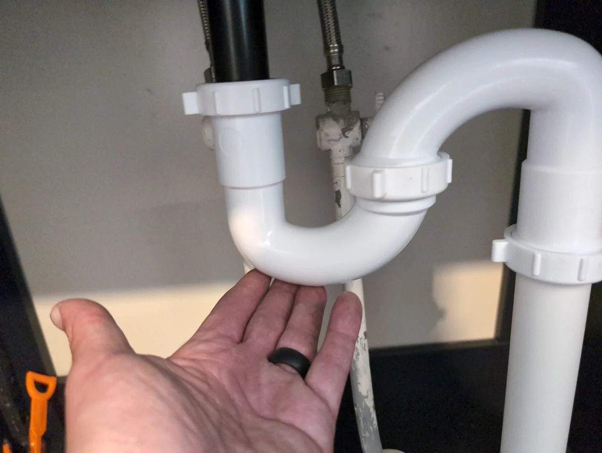 Checking beneath a sink drain trap for leaks during a home inspection